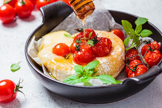 Baked Camembert or Brie cheese with tomatoes and honey in black pan