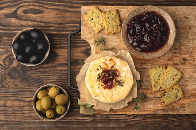 Baked camembert cheese with jam and snacks, on a wooden board, top view