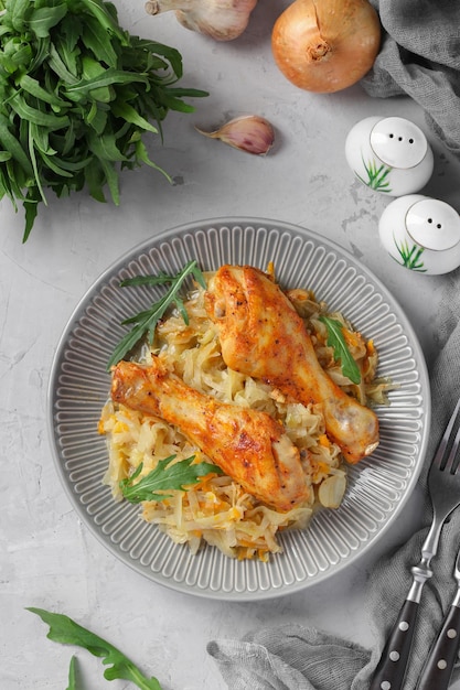 Baked chicken drumsticks with cabbage and garlic on gray plate Top view