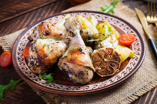 Baked chicken legs with slice potatoes and herbs. Barbecue chicken drumsticks on wooden table.