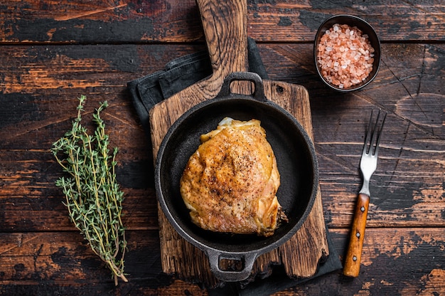 Baked chicken thigh in a pan with rosemary and salt. Dark Wooden table. Top View.