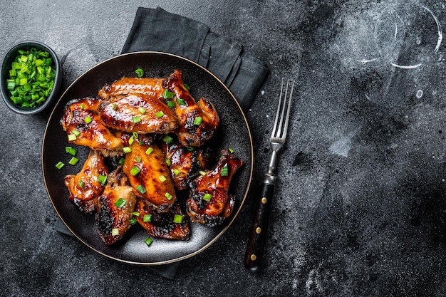 Baked chicken wings with sweet chili sauce in a plate Black background Top view Copy space