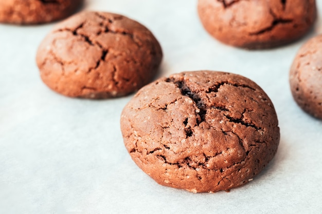 Baked cracked round chocolate cookies on a baking sheet with parchment paper just taken out of the oven. Tea snack. Selective focus. Closeup view