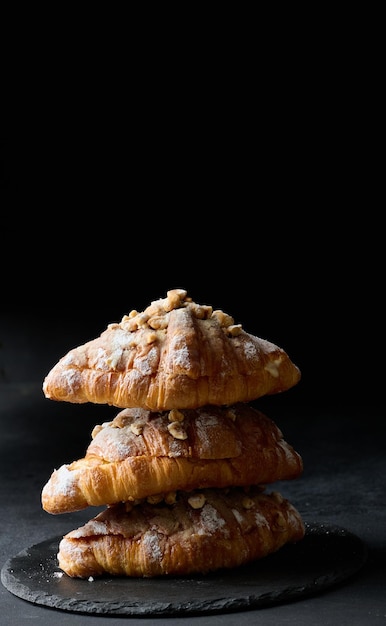 Baked croissant on a board and sprinkled with powdered sugar black table Appetizing pastries for breakfastx9