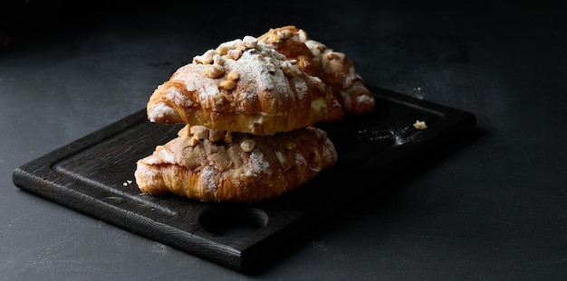 Baked croissant on a board and sprinkled with powdered sugar black table Appetizing pastries for breakfastx9