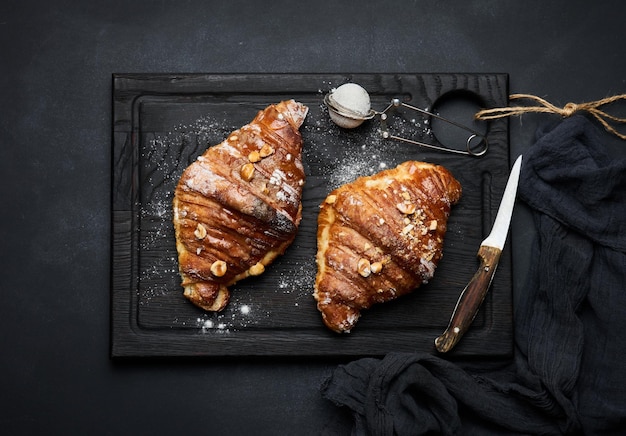 Baked croissant on a wooden board and sprinkled with powdered sugar black table Appetizing pastries for breakfast