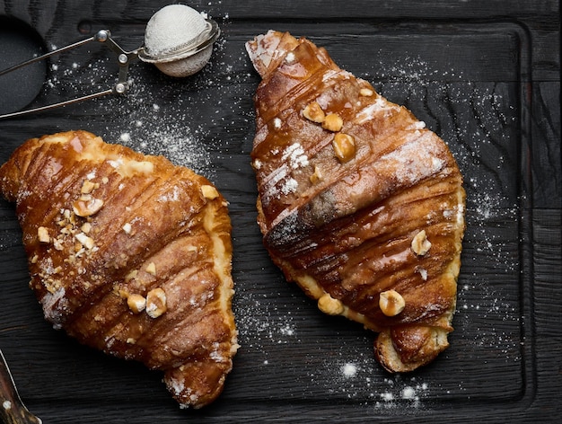 Baked croissant on a wooden board and sprinkled with powdered sugar black table Appetizing pastries for breakfast