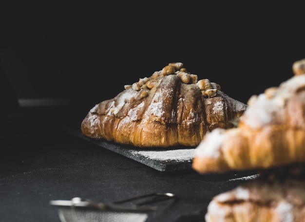 Baked croissant on a wooden board and sprinkled with powdered sugar black table Appetizing pastries for breakfast