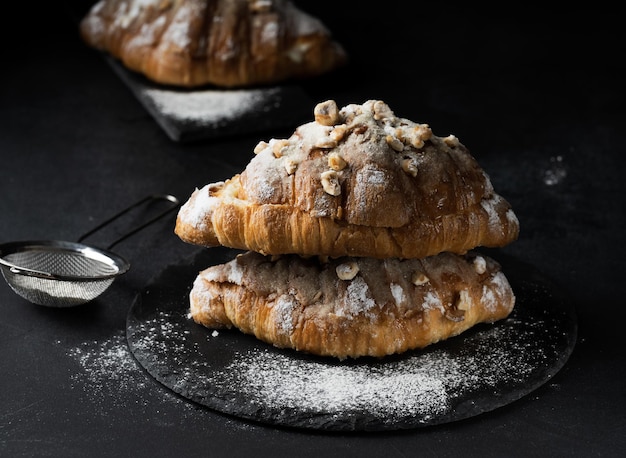 Baked croissant on a wooden board and sprinkled with powdered sugar black table Appetizing pastries for breakfast