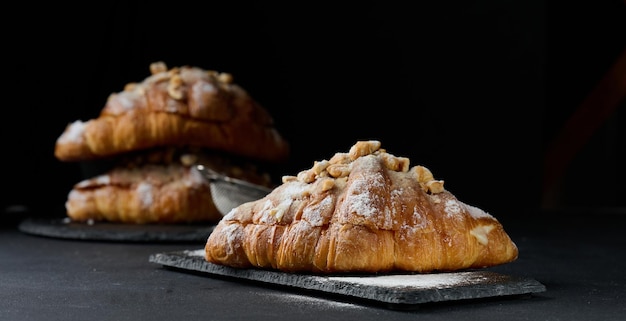 Baked croissant on a wooden board and sprinkled with powdered sugar black table Appetizing pastries for breakfast