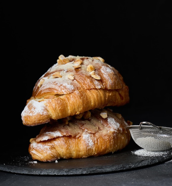 Baked croissant on a wooden board and sprinkled with powdered sugar black table Appetizing pastries for breakfast