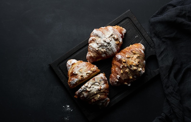 Baked croissants on a black wooden board sprinkled with powdered sugar top view