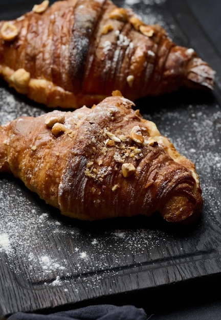 Baked croissants on a black wooden board sprinkled with powdered sugar