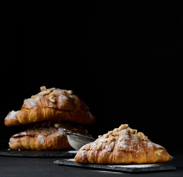 Baked croissants on a black wooden board sprinkled with powdered sugar