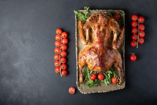 Baked duck stuffed with apples on gray plate with tomato cherry on a dark background