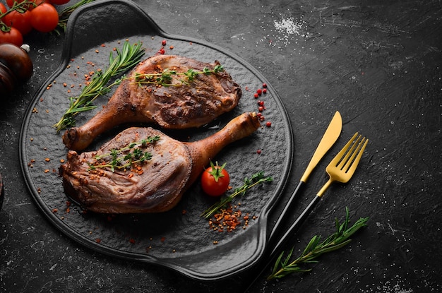 Baked duck thigh with spices and rosemary. Barbecue meat. Top view. Flat lay top view on black stone cutting table.