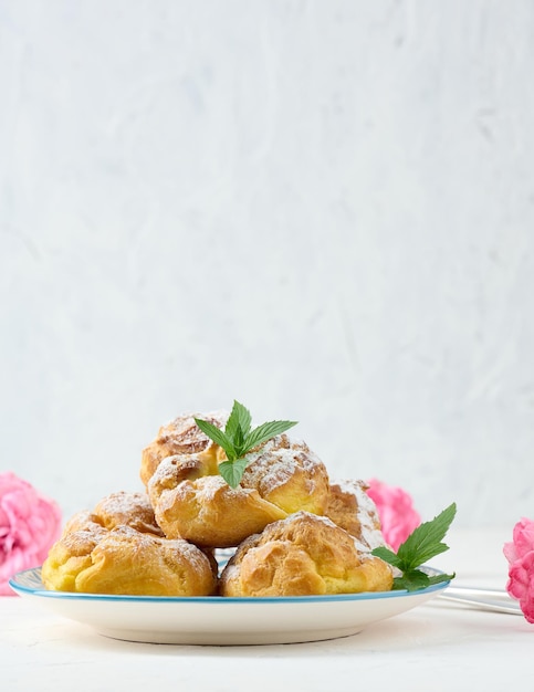 Baked eclairs with custard cream on a round plate sprinkled with powdered sugar