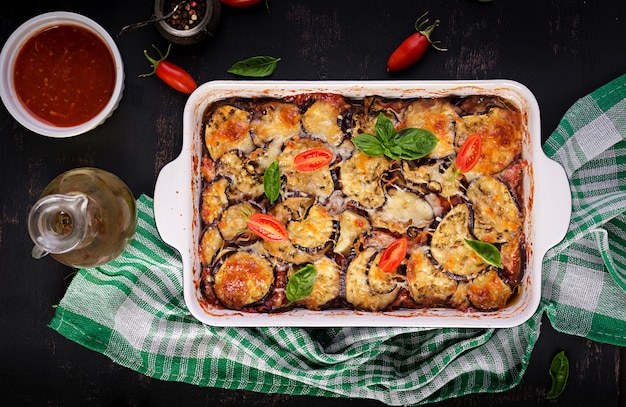 Baked eggplant with cheese on a dark wooden table. Parmigiana melanzane. Top view. Italian cuisine. 