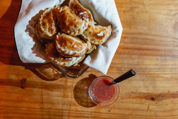 Baked empanadas on a wooden table with hot sauce