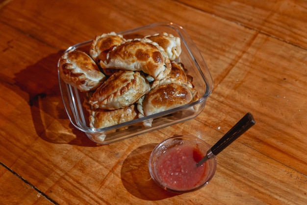 Baked empanadas on a wooden table with hot sauce