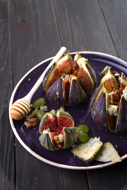 Baked figs with goat cheese, walnuts and honey on ceramic plate and brown wooden background