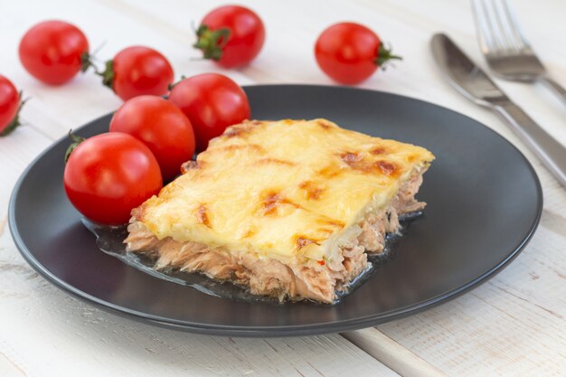 Baked fish casserole under cheese on white wooden table