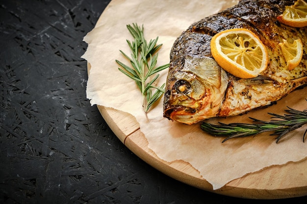 Baked fish in oven with lemon and rosemary laid out cutting board and parchment paperOn dark background