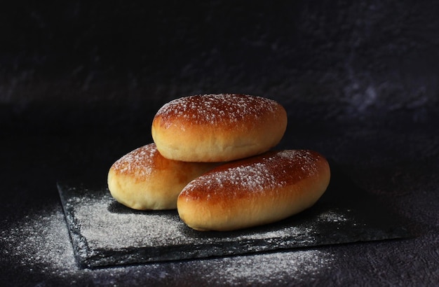 Baked homemade pies in a row on a black slide board on a dark background