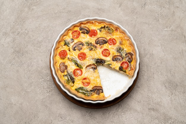 Baked homemade quiche pie in ceramic baking form on concrete background