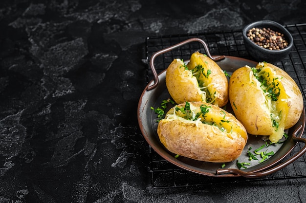 Baked Jacket potatoes with cheese herbs and butter Black background Top view Copy space