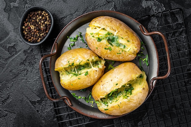 Baked Jacket potatoes with cheese herbs and butter Black background Top view