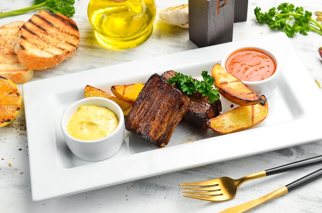 Baked juicy pork ribs with potatoes and sauce. Top view. On a white plate.