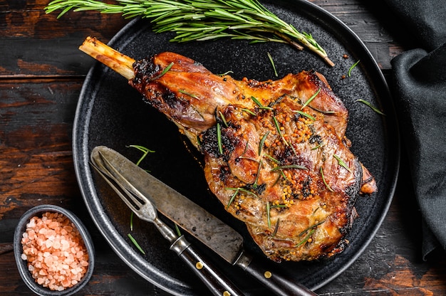 Baked lamb, sheep leg with rosemary.  Dark wooden background. Top view.