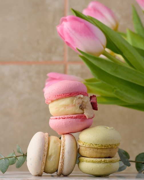 Baked macarons with different flavors on the table behind a bouquet of tulips