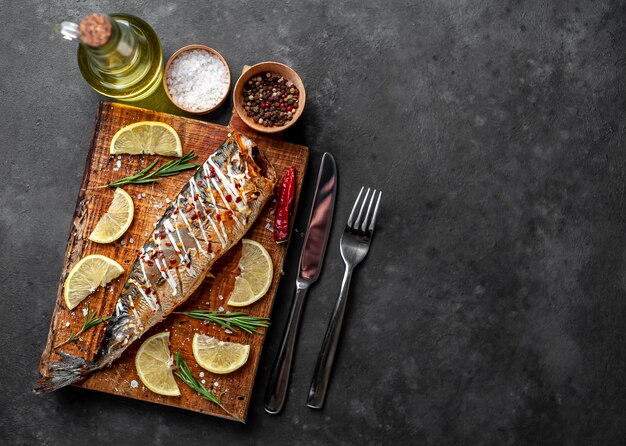 baked mackerel on a cutting board with lemon and spices on a stone background 