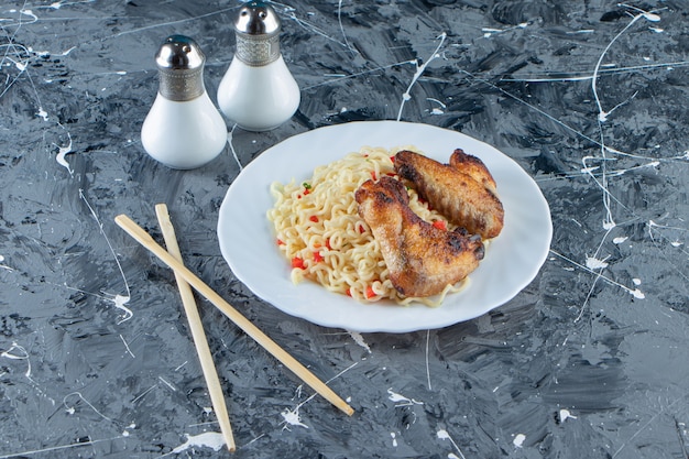 Baked meat and noodle on a plate next to salt and chopstick, on the marble surface.