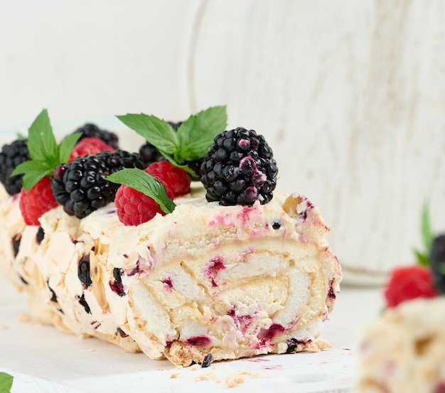 Baked meringue roll with cream and fresh fruits on a white wooden board delicious dessert