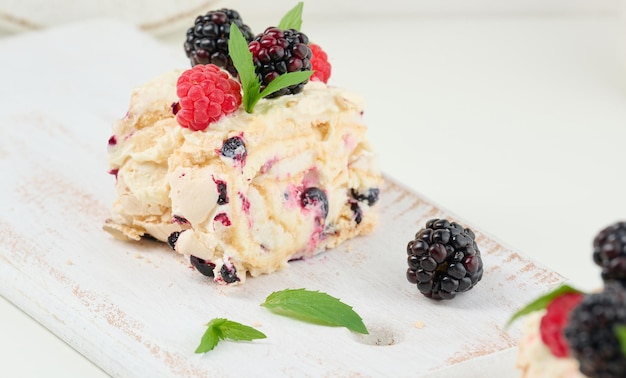 Baked meringue roll with cream and fresh fruits on a white wooden board delicious dessert