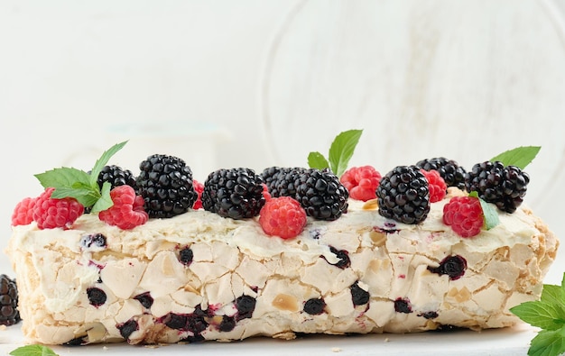 Baked meringue roll with cream and fresh fruits on a white wooden board delicious dessert