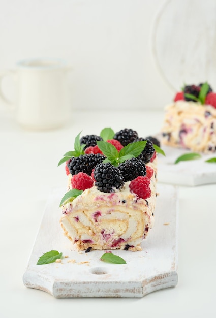 Baked meringue roll with cream and fresh fruits on a white wooden board delicious dessert