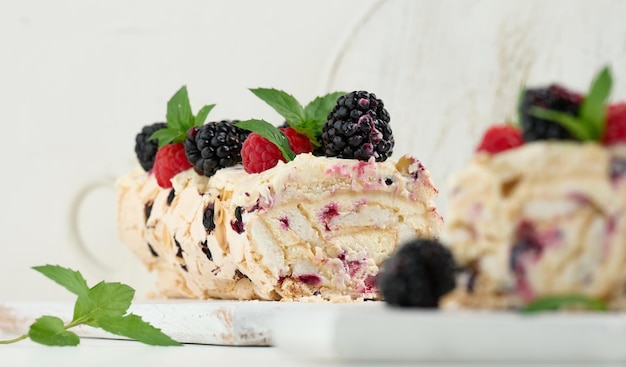 Baked meringue roll with cream and fresh fruits on a white wooden board delicious dessert