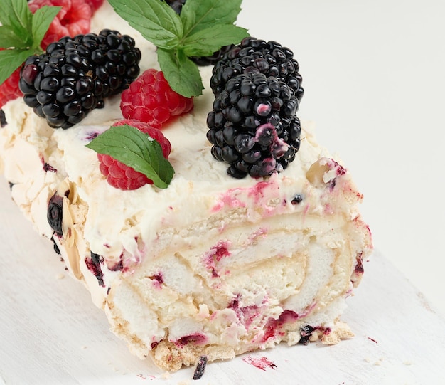 Baked meringue roll with cream and fresh fruits on a white wooden board delicious dessert