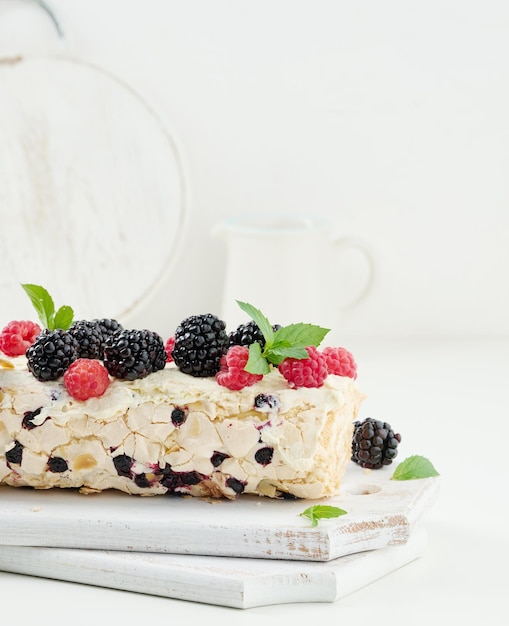 Baked meringue roll with cream and fresh fruits on a white wooden board delicious dessert