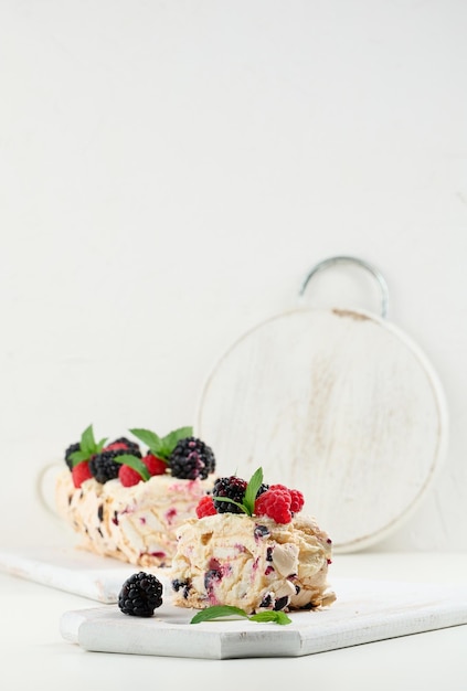 Baked meringue roll with cream and fresh fruits on a white wooden board delicious dessert