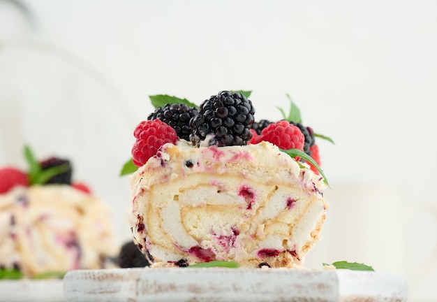 Baked meringue roll with cream and fresh fruits on a white wooden board delicious dessert