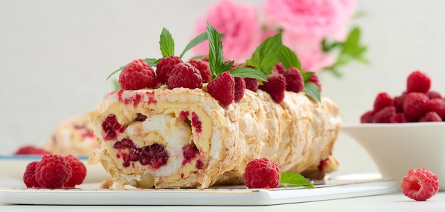 Baked meringue roll with cream and fresh fruits on a white wooden board