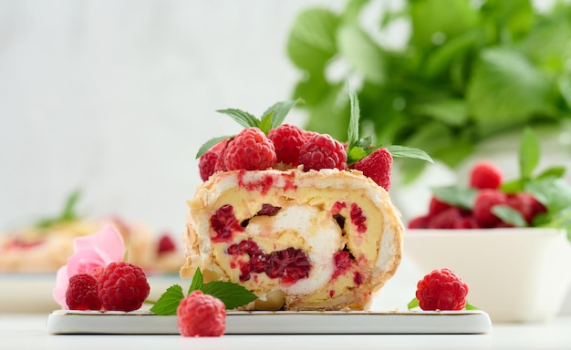 Baked meringue roll with cream and fresh red raspberry on a white board