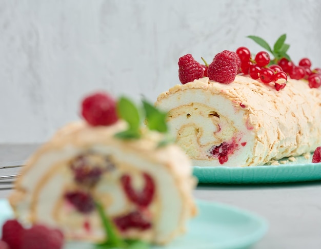 Baked meringue roll with red berries on a round plate white background