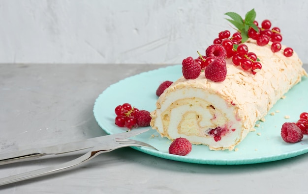 Baked meringue roll with red berries on a round plate white background