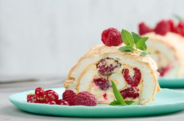 Baked meringue roll with red berries on a round plate white background